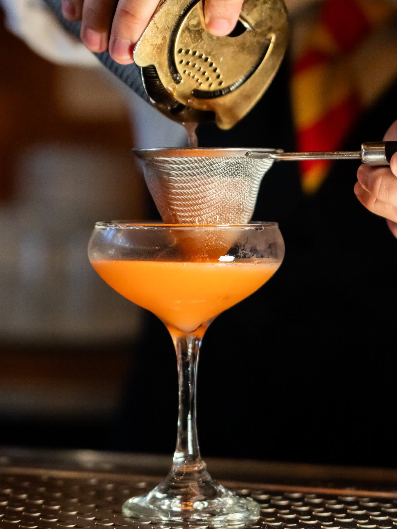 Double-straining a cocktail into a chilled coupe glass.