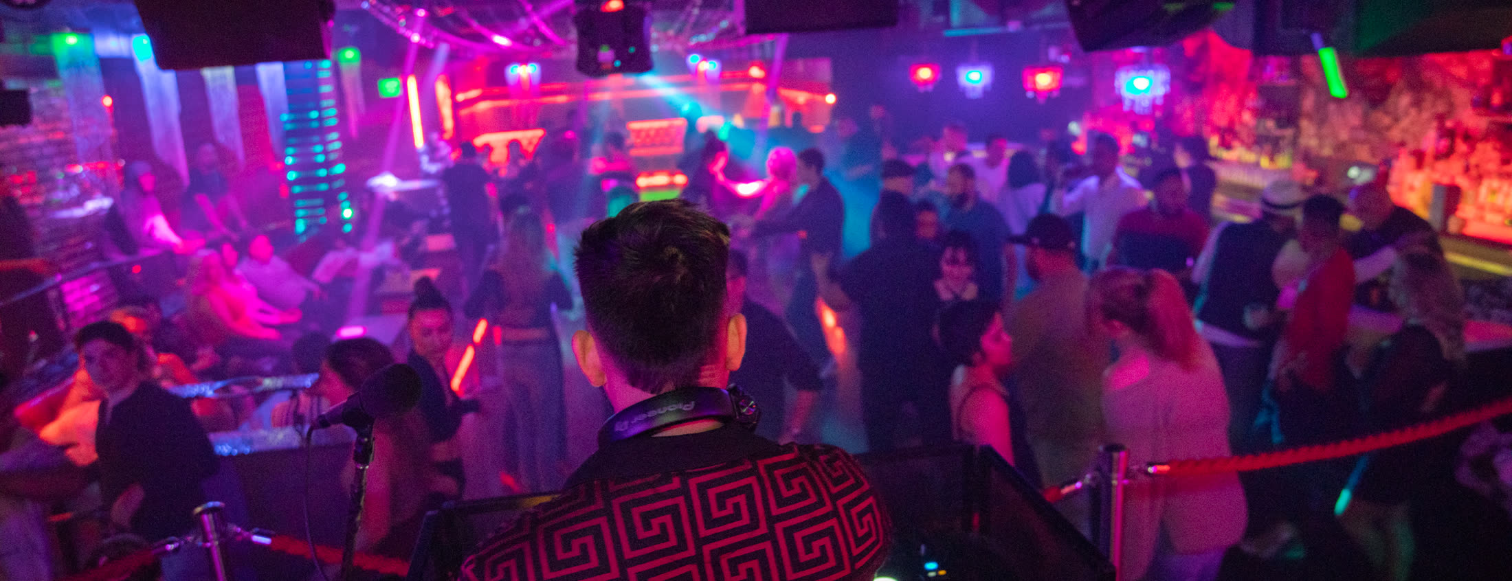 DJ facing a packed, neon-lit dance floor inside Caf&eacute; Sevilla Nightclub
