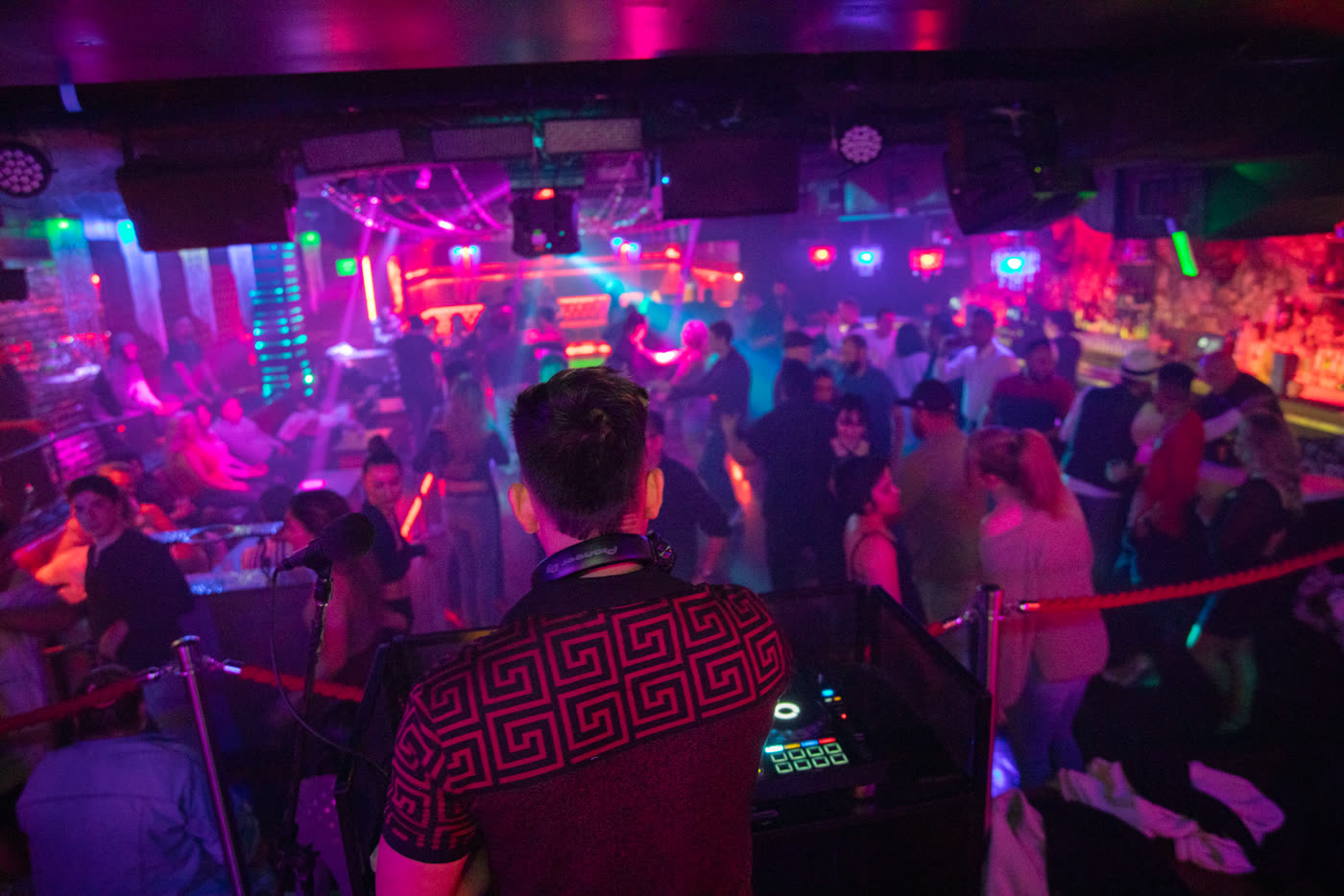 DJ overlooking a packed, colorfully lit dance floor.