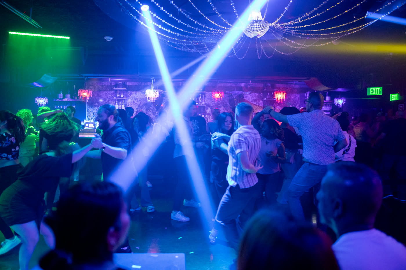Dancers moving under crossing blue lasers and a crystal chandelier.